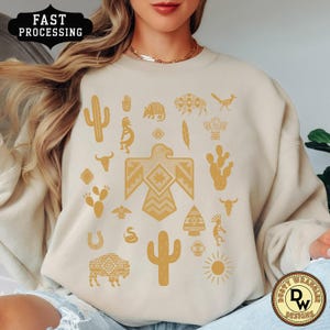 May include: Beige sweatshirt with a collection of Southwestern-inspired illustrations in a golden-yellow color. The design includes cacti, birds, and geometric patterns. The words "FAST PROCESSING" are in a black banner.