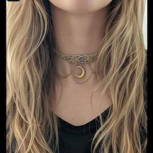 Könnte beinhalten: Beige Makramee-Halskette mit einem goldfarbenen Halbmond-Anhänger. Die Halskette hat einen zentralen blauen Edelstein und zarte Kettenakzente, die einen Bohemian-Stil erzeugen.