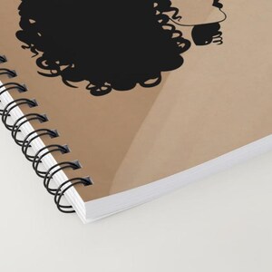 May include: A brown spiral notebook with a black silhouette of a person with curly hair. The notebook is closed and the spine is visible.