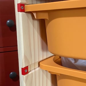 May include: A wooden cabinet with two orange plastic storage bins. The bins are attached to the cabinet with red brackets and screws.