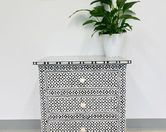 May include: A white and black geometric patterned nightstand with four drawers and white knobs. The nightstand is sitting on a patterned rug.
