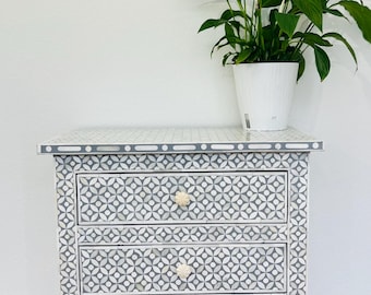 May include: A white and gray four-drawer dresser with a geometric pattern. The dresser has white knobs and a gray trim around the top.