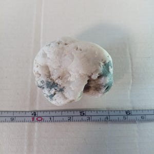 Può includere: Un sasso bianco e verde con una superficie ruvida. Il sasso ha un diametro di circa 4 cm.