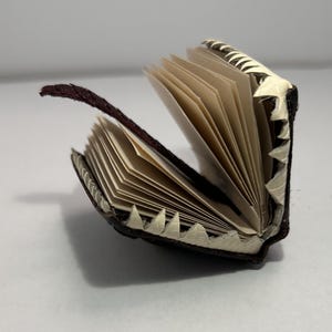 May include: A small, brown leather-bound journal with a white, decorative edge. The journal is open and the pages are blank.