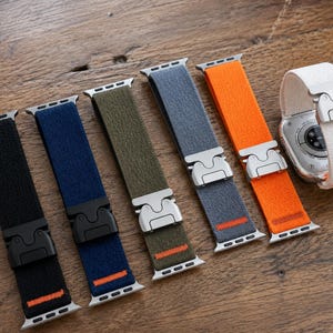 Puede incluir: Una colección de seis correas elásticas para reloj con hebillas metálicas. Las correas vienen en negro, azul marino, verde oliva, gris, naranja y blanco. Cada correa incluye un conector metálico y una pequeña costura de acento naranja.