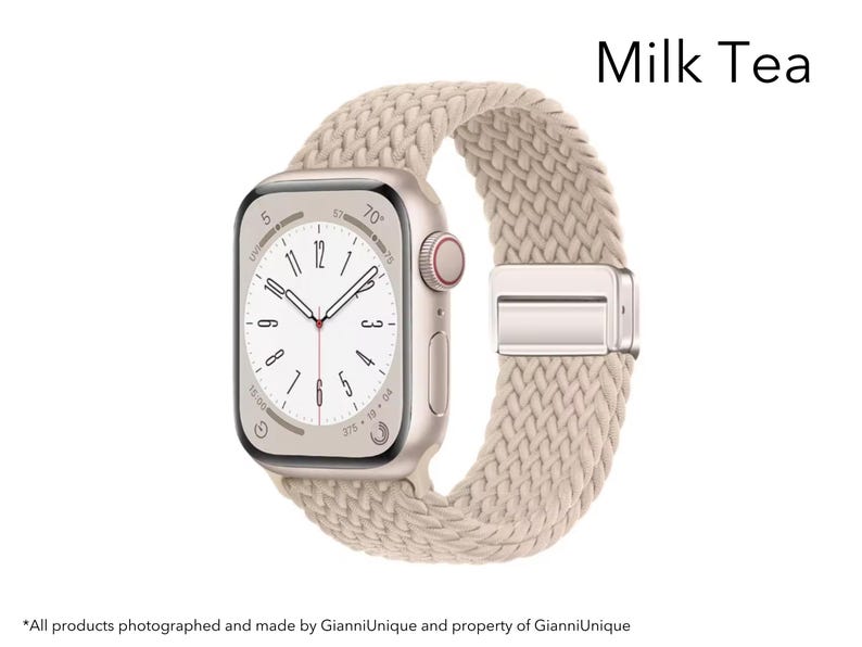 May include: A smartwatch with a rectangular gold-tone case and a beige braided fabric band featuring a metallic clasp. The watch face displays a white dial with black numerals and hands. The text Milk Tea is visible in the upper right corner.