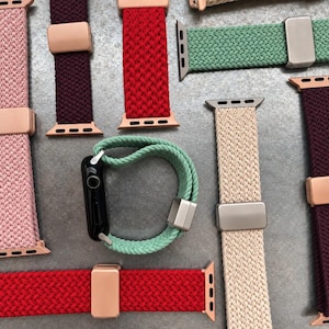 Peut inclure: Une collection de bracelets de montre tressés dans diverses couleurs, notamment rose, bordeaux, rouge, vert clair et beige. Chaque bracelet comporte un connecteur métallique et une boucle coulissante réglable assortie.