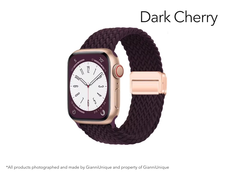 May include: A smartwatch with a gold-tone case and a dark cherry braided solo loop band. The watch face displays a white dial with black numerals and hands, showing the text Dark Cherry. The band features a metallic gold-tone adjustable clasp.