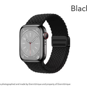 May include: A black smartwatch with a rectangular screen displaying a clock face with white hands and a red second hand. The watch features a textured, braided black band with a matching black magnetic clasp. The word Black is printed above.