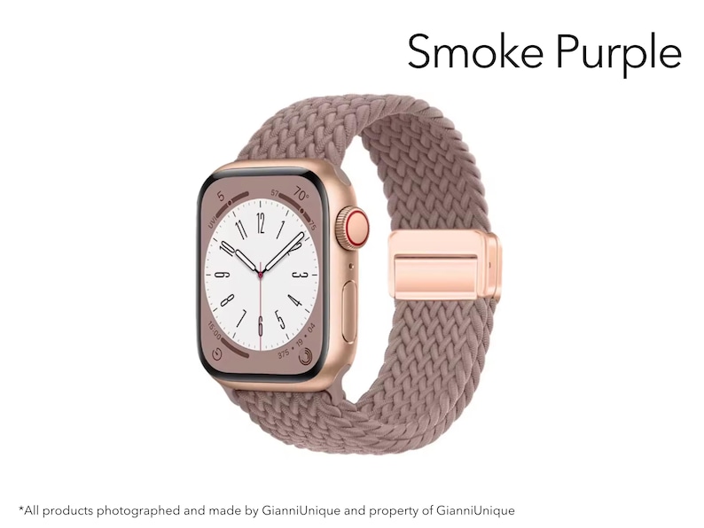 May include: A smartwatch with a metallic rose gold case and a smoke purple braided solo loop band. The watch face displays a white dial with black numerals and hands. The text Smoke Purple is visible in the upper right corner of the image.
