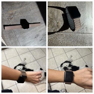 Op de afbeelding: Een zwarte smartwatch met een roségouden metalen band, weergegeven op een houten oppervlak. De band is gemaakt van kleine, verbonden metalen schakels. Het horloge wordt ook om een pols gedragen.