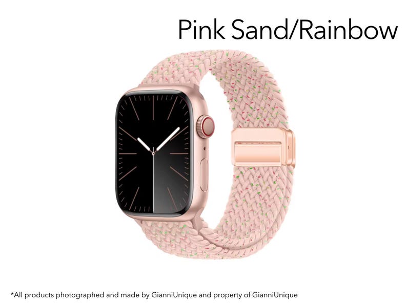 May include: A smartwatch with a rose gold case and a black screen featuring white clock hands. The watch band is a braided pink sand material with subtle rainbow-colored flecks. The text Pink Sand/Rainbow is displayed above the watch.