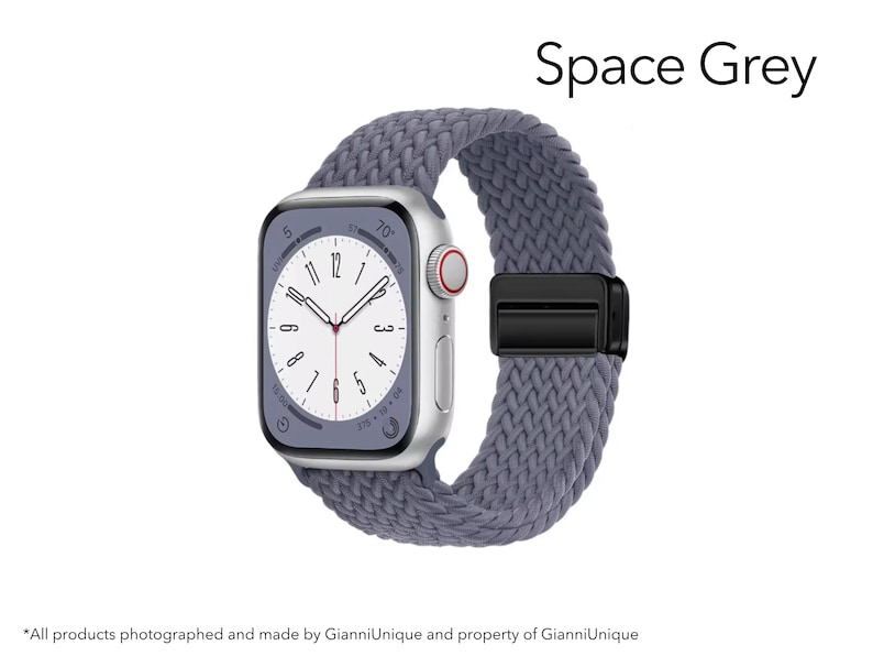 May include: A smartwatch with a rectangular silver case and a white analog clock face featuring black numerals. The watch is attached to a textured, braided grey strap secured by a black metal clasp. The text Space Grey appears above the watch.