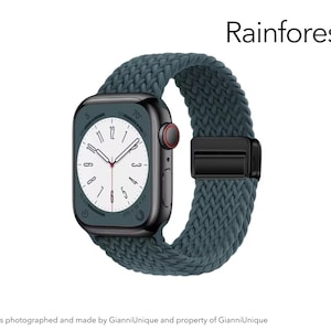 May include: A smartwatch with a dark metallic rectangular case and a dark teal braided solo loop band. The watch face displays a white dial with black numerals and hands. The word Rainforest is printed in black text above the watch.