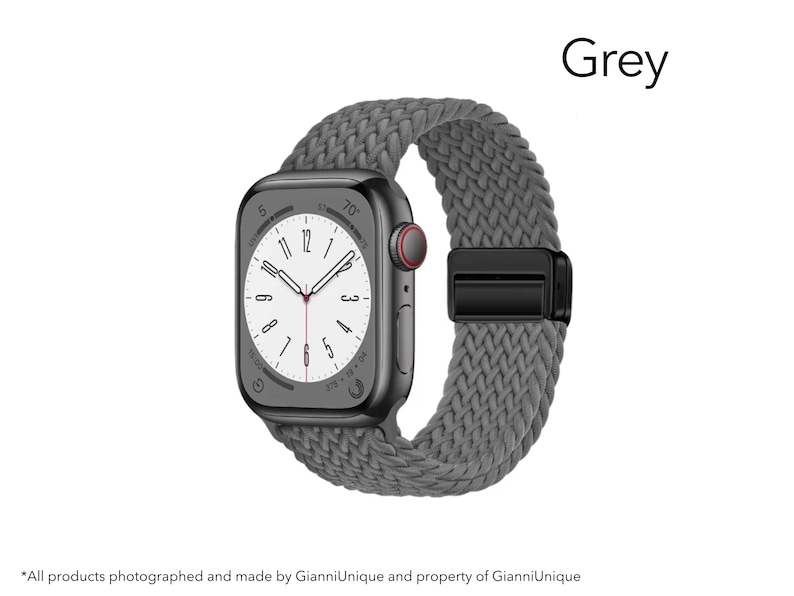 May include: A smartwatch with a dark grey rectangular case and a grey braided elastic watch band. The watch face displays a white background with black numerals and hands. A black magnetic clasp secures the band. The word Grey is visible.