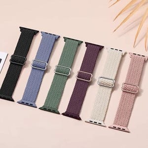 May include: Seven different colored woven nylon watch bands for Apple Watch. The bands are black, light blue, green, purple, cream, and pink.