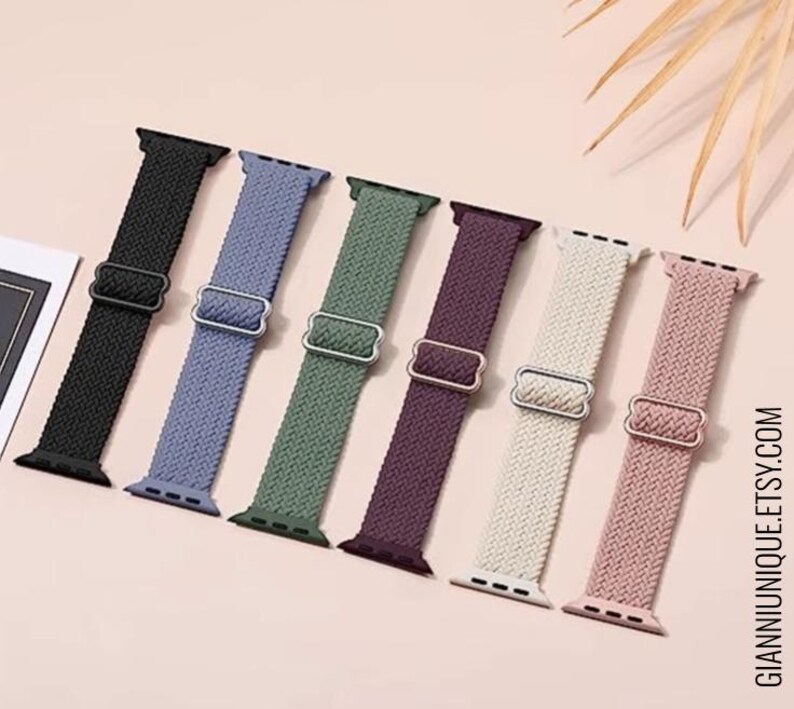 May include: Seven different colored woven nylon watch bands for Apple Watch. The bands are black, light blue, green, purple, cream, and pink.