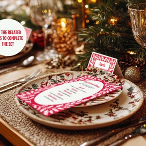 May include: A red and white Christmas menu card with a floral design sits on a white plate with a floral pattern. The plate is on a brown woven placemat. A glass of water and a gold candle holder are in the background. The text on the card reads "Christmas Menu".