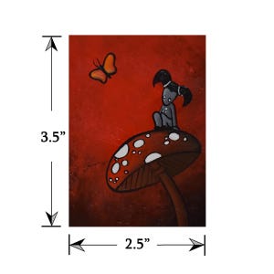 May include: A whimsical painting featuring a figure with black pigtails seated on a mushroom with white spots. An orange butterfly hovers nearby against a red background. The artwork measures 3.5 inches by 2.5 inches.