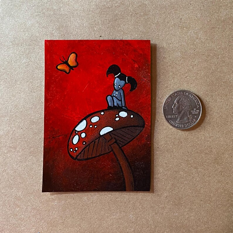 May include: A small painting featuring a whimsical scene. A blue figure sits atop a mushroom with white spots against a red background. An orange butterfly flies nearby. A U.S. quarter is included for size reference.