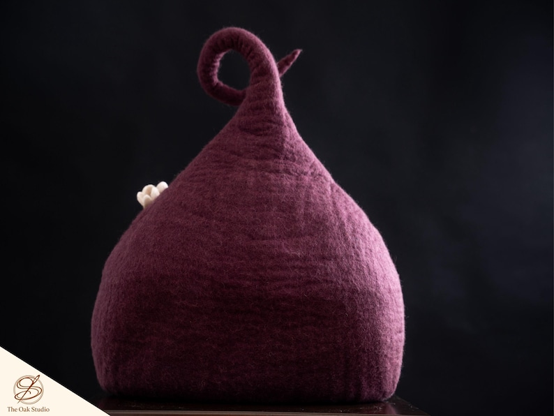 Peut inclure: Un chapeau en feutre de couleur prune profonde avec un sommet haut, pointu et recourb&eacute;, orn&eacute; d'une petite fleur de couleur claire sur le c&ocirc;t&eacute;. Le chapeau pr&eacute;sente une surface textur&eacute;e et dense en laine avec une forme conique distincte.