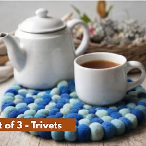 May include: A white teapot and mug of tea rest on a blue and teal trivet. The trivet is made of felted wool balls. The image includes a basket of flowers and the text "Set of 3 - Trivets".
