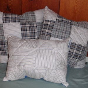 May include: Three decorative pillows with a patchwork design. The pillows are made of blue and white plaid fabric and white fabric with blue stripes. The pillows are arranged on a light blue surface.