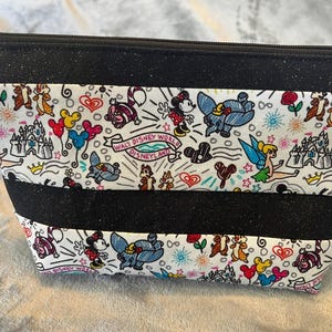 May include: A black glittery zipped pouch with a white panel featuring Disney characters including Mickey Mouse, Dumbo, and Chip and Dale. The pouch has a silver ring attached to the side and the words "Walt Disney World Disneyland".