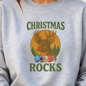 May include: Heather grey sweatshirt with a graphic featuring a reindeer with a red nose and the text "CHRISTMAS ROCKS" in green. The reindeer is inside a yellow circle with a forest background and colorful gemstones.