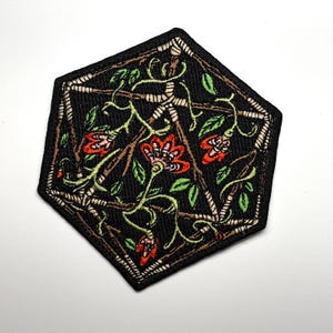 Könnte beinhalten: Schwarzer, geometrischer Aufnäher mit floralem Design. Der Aufnäher hat eine Pentagonform mit schwarzem Hintergrund, braunen Ranken, roten Blumen und grünen Blättern. Die Ränder sind weiß umrandet.