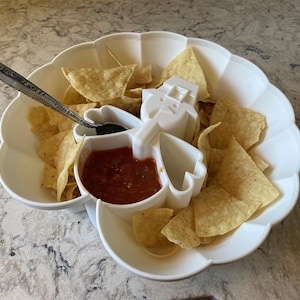 May include: White ceramic serving dish shaped like a person with a separate compartment for salsa and a large compartment for tortilla chips.