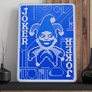 Könnte beinhalten: Ein rechteckiges Wandbild mit einem verpixelten blau-weißen Design einer Narrenfigur. Das Wort JOKER ist in einer blockartigen Schrift vertikal auf der linken und rechten Seite der zentralen Narrenfigur vor einem blauen Hintergrund gedruckt.