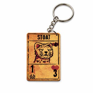Puede incluir: Un llavero rectangular con una ilustración en pixel art de un armiño sobre una tarjeta de color tostado con aspecto desgastado. La tarjeta muestra el texto STOAT, un icono de gota de sangre, una huella, el número 1 y un icono de corazón rojo con el número 3.