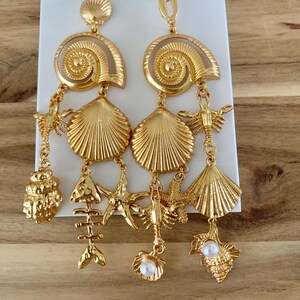 Puede incluir: Pendientes dorados con colgantes de conchas marinas, estrellas de mar y langostas. Los pendientes tienen un dise&ntilde;o en espiral en la parte superior y un acento de perla. El logotipo de ZARA es visible en el fondo.