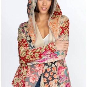 May include: A hooded jacket with a patchwork floral design. The jacket features a variety of floral patterns in shades of red, pink, beige, and gray. The hood is lined with a soft, cream-colored material. The jacket is open in the front and has long sleeves.