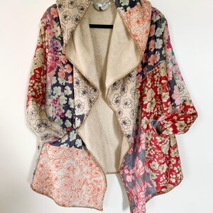 May include: A patchwork floral print jacket with a beige interior. The jacket features a shawl collar and pockets. The floral patterns include red, pink, blue, and beige. The jacket is hanging on a black hanger against a white background.