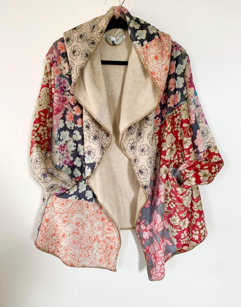 May include: A patchwork floral print jacket with a beige interior. The jacket features a shawl collar and pockets. The floral patterns include red, pink, blue, and beige. The jacket is hanging on a black hanger against a white background.