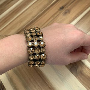 Op de afbeelding: Een armband van goudkleurige toon met meerdere rijen amberkleurige strass.
