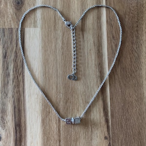 May include: A silver chain necklace with a charm that spells out "CD" in block letters. The charm has a small crystal in the center.