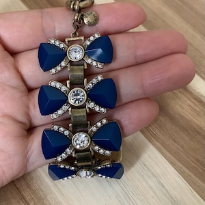 Op de afbeelding: Een gouden armband met drie marineblauwe strikcharms versierd met heldere strass steentjes. De armband heeft een J.Crew logo bedel.