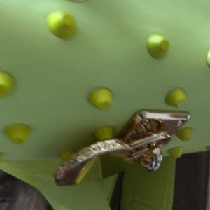 May include: A lime green bag featuring a series of evenly spaced, matching lime green conical studs across its surface. The bag is secured with a polished gold-tone metal turn-lock closure mechanism that is positioned on the front flap.