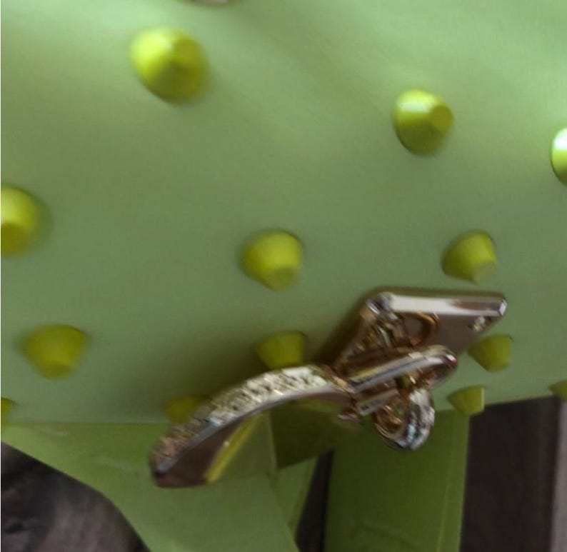 May include: A lime green bag featuring a series of evenly spaced, matching lime green conical studs across its surface. The bag is secured with a polished gold-tone metal turn-lock closure mechanism that is positioned on the front flap.