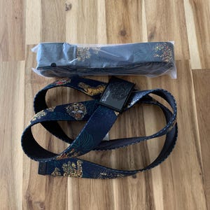 May include: A navy blue belt with a tiger and floral pattern. The belt is made of a durable material and features a black buckle. The belt is new and still in its original packaging.