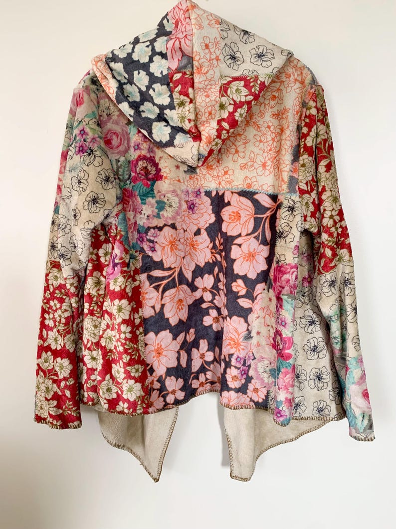 May include: A hooded jacket with a patchwork design featuring various floral patterns in shades of red, pink, and cream. The jacket has a beige lining and a unique, open front design. The hood is also patterned with flowers.