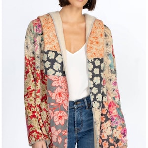 May include: A hooded patchwork jacket with a floral pattern in shades of red, pink, orange, and blue. The jacket has a beige lining and is worn over a white top and blue jeans. The jacket's design is a mix of floral prints.