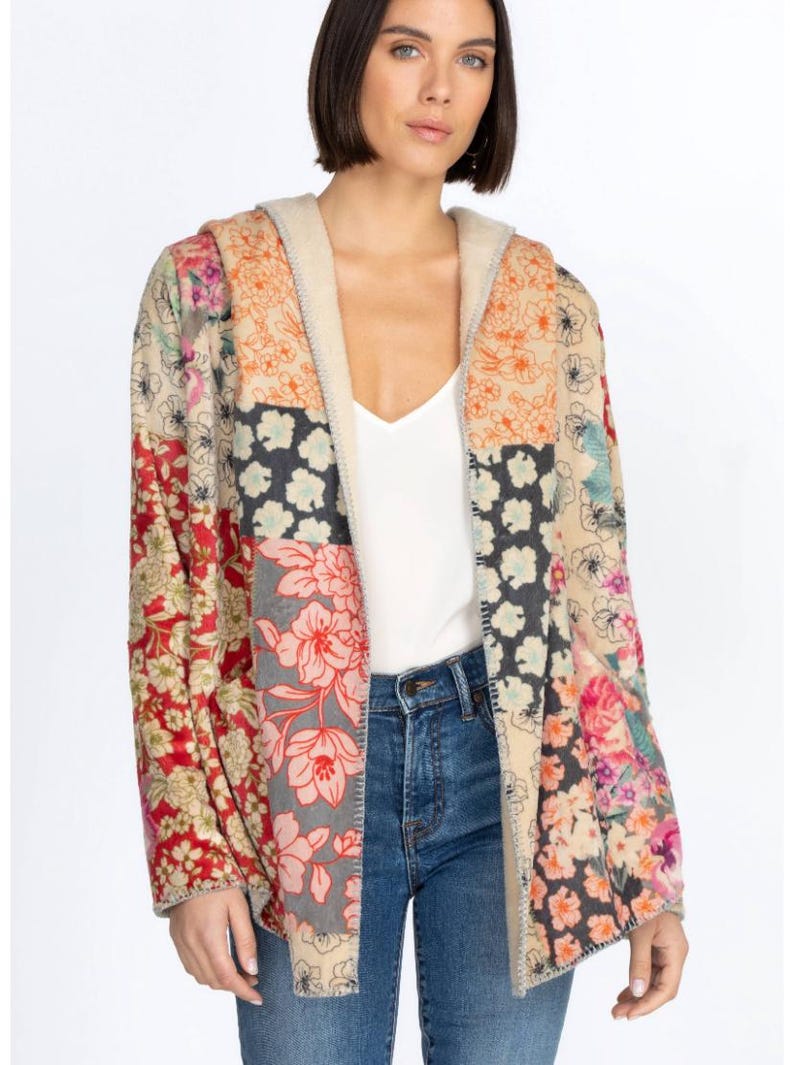 May include: A hooded patchwork jacket with a floral pattern in shades of red, pink, orange, and blue. The jacket has a beige lining and is worn over a white top and blue jeans. The jacket's design is a mix of floral prints.