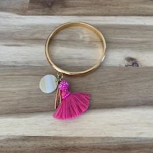 May include: A gold bangle bracelet with a pink tassel charm and a white shell charm.