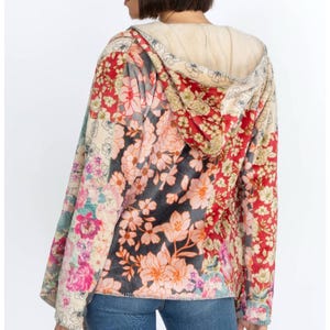 May include: A floral print hoodie with a cream-colored hood lining. The jacket features a patchwork design with various floral patterns in red, pink, and cream colors. The model is wearing blue jeans.