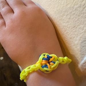 Könnte beinhalten: Ein gelbes Gummiband-Armband mit einem blauen, orangenen und gelben Zentrum.