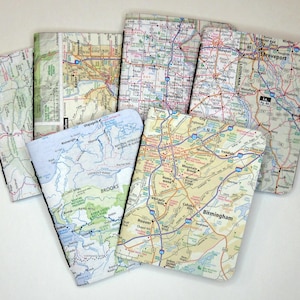 May include: A collection of rectangular notebooks, each covered with a different vintage map design. The maps feature various cities and regions, with a mix of colors and detailed road networks. The notebooks are arranged in a fan shape.